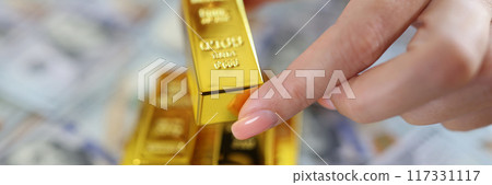 Woman hand holding small gold ingots, cash on background Woman hand holding small gold ingots, cash on background 117331117