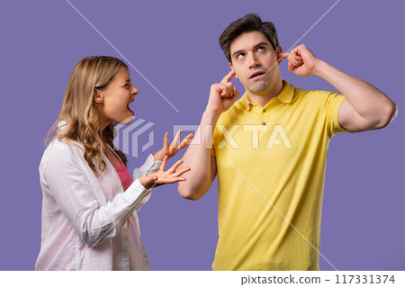 Grumpy woman quarrels on husband or boyfriend On violet. Tired man covers ears 117331374