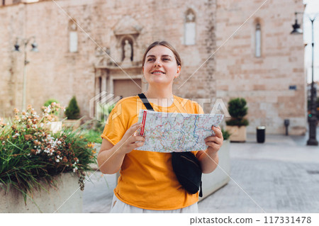 Young beautiful 30s woman looking city map at street, old town. Attractive young female tourist is exploring new city. Traveling Europe, High quality photo 117331478