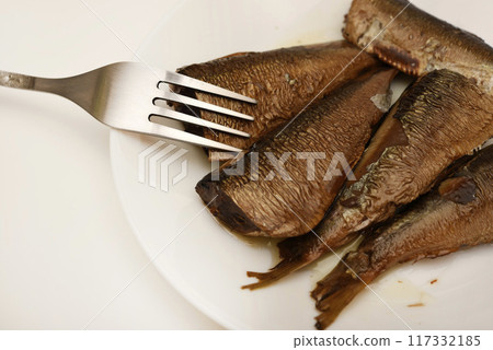 Sprats on a white plate with a fork. Canned fish in oil. Fish appetizer. Sprats on a white plate with a fork. Canned fish in oil. Fish appetizer. 117332185