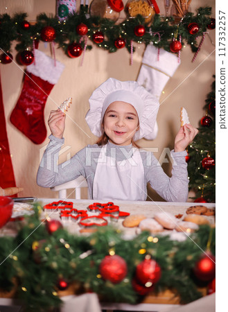 A girl in a chef's hat smiles and shows Christmas gingerbread cookies in the shape of a Christmas tree. 117332257