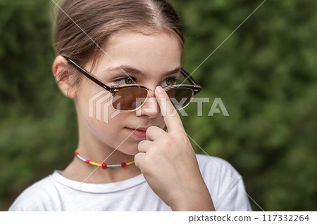 Little girl holds sunglasses with her finger and looks into the distance 117332264