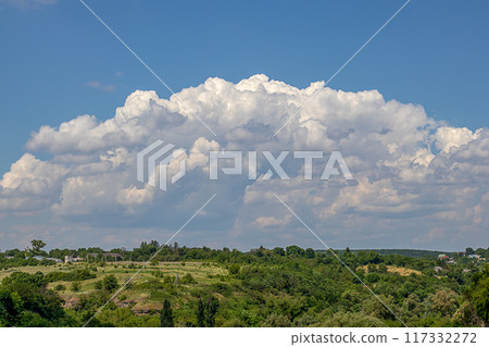 A large cumulus rain cloud on a blue sky over a green earth. 117332272
