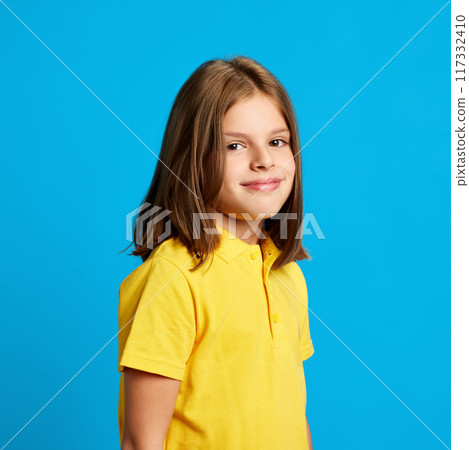 Side view portrait of beautiful teen girl wearing yellow polo shirt, posing with little tender smile against blue studio background Side view portrait of beautiful teen girl wearing yellow polo shirt, posing with little tender smile against blue studio background 117332410