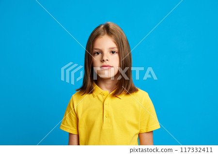 Portrait of young 9 years old girl with brown hair, in pink polo shirt looking at camera with calm face, posing against blue studio background Portrait of young 9 years old girl with brown hair, in pink polo shirt looking at camera with calm face, posing against blue studio background 117332411