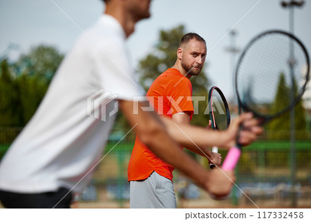 Focus on bearded man in orange t-shirt showing focus and concentration during intense outdoor game with his friends. Competitive spirit. 117332458