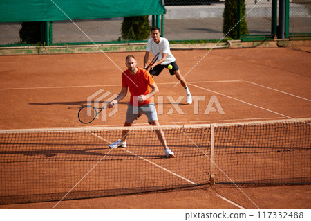 Concentrated men, tennis players in motion on open air clay court, showing skills, energy and good teamwork during game. 117332488