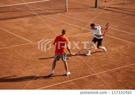 Two men, tennis players in motion on outdoor clay court, showing game skills and teamwork cooperation, playing with focus 117332492