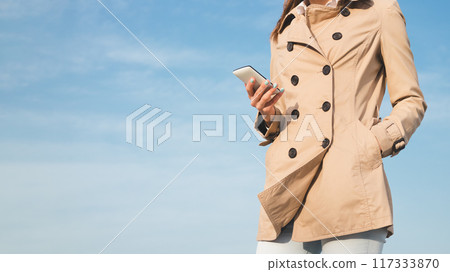 A woman is wearing a coat and holding a cell phone A woman is wearing a coat and holding a cell phone 117333870