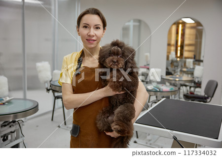 Portrait of happy friendly smiling groomer holding cute dog client 117334032