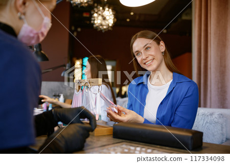 Happy female client selecting nail polish on color palette for manicure 117334098