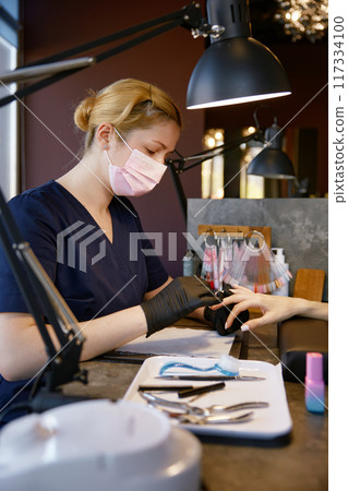 Manicurist in protective facial mask and gloves providing safety manicure 117334100