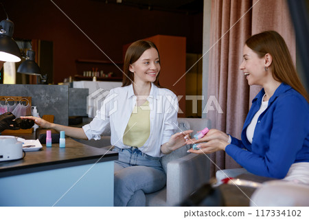 Young woman advising friend color of nail polish in spa salon 117334102