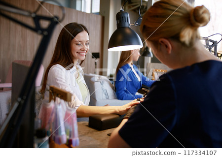 Happy laughing woman friends getting manicure and gossiping together Happy laughing woman friends getting manicure and gossiping together 117334107