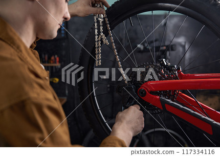 Man mechanic performing mountain bike maintenance fixing chain 117334116