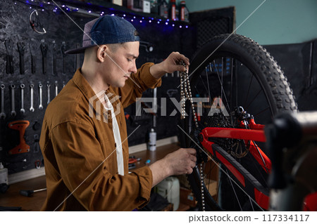 Man mechanic performing mountain bike maintenance fixing chain 117334117