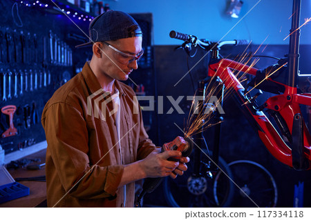 Young handsome man bike mechanic using circular saw for repair work 117334118