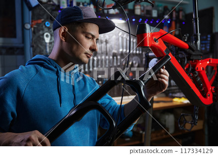 Young repairman adjusting suspension fork repairing bicycle at garage in evening Young repairman adjusting suspension fork repairing bicycle at garage in evening 117334129