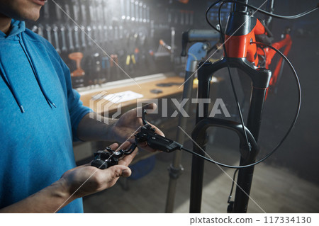 Male mechanic engaged in installation of braking system at bicycle garage 117334130