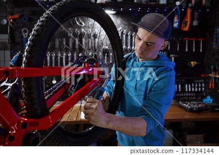 Closeup of hipster man bike mechanic removing rear wheel at garage workshop Closeup of hipster man bike mechanic removing rear wheel at garage workshop 117334144