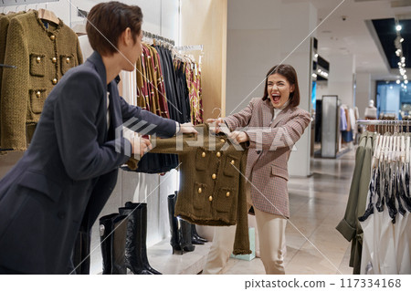 Two furious women shopaholic fighting for clothes on sale Two furious women shopaholic fighting for clothes on sale 117334168