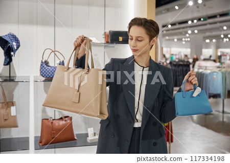 Portrait of young woman choosing new fashion leather bag at boutique 117334198