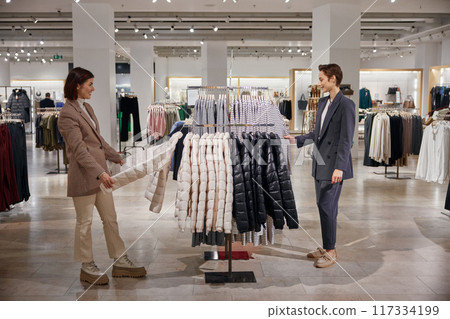 Two young female friends shopping together choosing clothes at store Two young female friends shopping together choosing clothes at store 117334199