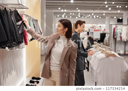 Two elegant woman enjoying shopping at fashion clothes boutique Two elegant woman enjoying shopping at fashion clothes boutique 117334214