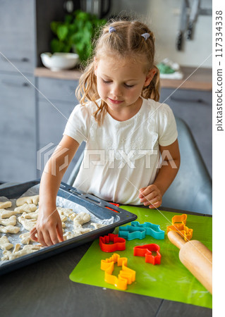 Little girl making cookie with dough using animal shape cutters in the home kitchen, Family concept Little girl making cookie with dough using animal shape cutters in the home kitchen, Family concept 117334338