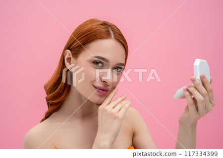 Ginger woman with bare shoulders with cream powder in hands Ginger woman with bare shoulders with cream powder in hands 117334399