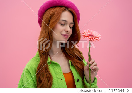 Pretty and sweet young woman in pink beret with a flower in hands looking dreamy Pretty and sweet young woman in pink beret with a flower in hands looking dreamy 117334440