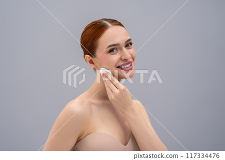 Young woman cleansing her face and looking relaxed Young woman cleansing her face and looking relaxed 117334476