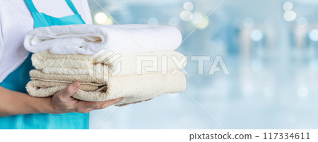 Cleaning lady in blue apron holding stack of clean towels. Cleaning lady in blue apron holding stack of clean towels. 117334611