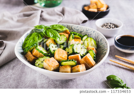 Fresh cucumber and fried tofu salad with basil leaves in bowl on table Fresh cucumber and fried tofu salad with basil leaves in bowl on table 117334653