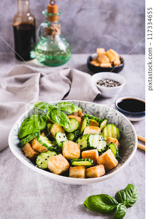 Fresh cucumber and fried tofu salad with basil leaves in bowl on table vertical view Fresh cucumber and fried tofu salad with basil leaves in bowl on table vertical view 117334655
