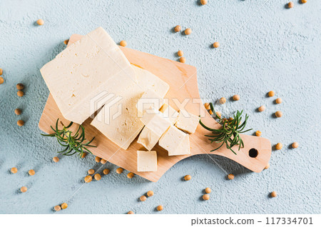 Close up of fresh slices of soy cheese tofu and rosemary on a wooden board on the table top view Close up of fresh slices of soy cheese tofu and rosemary on a wooden board on the table top view 117334701