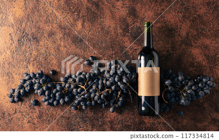 Blue grapes and bottle of red wine on a brown vintage background. Blue grapes and bottle of red wine on a brown vintage background. 117334814