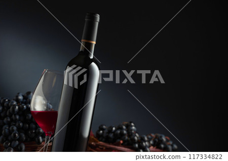 Bottle and glass of red wine with blue grapes on a black background. Bottle and glass of red wine with blue grapes on a black background. 117334822