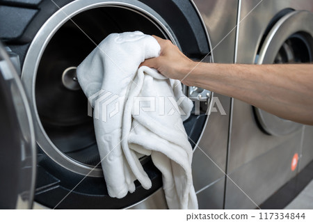 Anonymous man handling dirty laundry at self-service laundromat 117334844