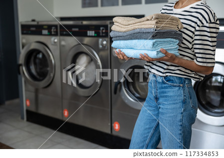 Unrecognizable woman carrying stack of towels at public laundromat Unrecognizable woman carrying stack of towels at public laundromat 117334853