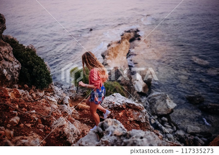 Woman exploring rocky coastline during sunset near calm ocean waters Woman exploring rocky coastline during sunset near calm ocean waters 117335273