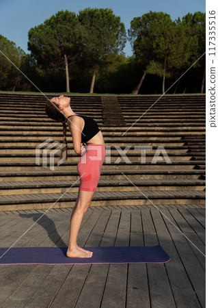 young redhead woman doing yoga exercises outdoors in park 117335516