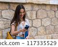 young woman with a folder is standing near wall sending a message 117335529