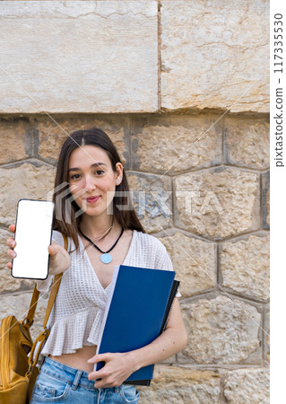 smiling student with a backpack showing a smartphone with white background 117335530