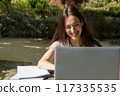 girl with laptop in a videoconference smiling in the park  117335535