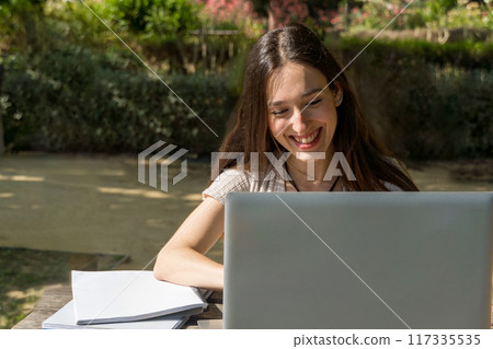 girl with laptop in a videoconference smiling in the park  117335535