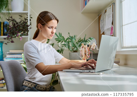 Female teenager college student studying at home sitting at desk with laptop 117335795