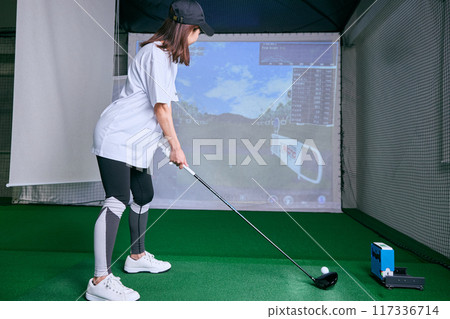 A woman practicing at an indoor golf driving range 117336714