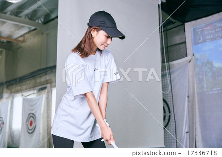 A woman practicing at an indoor golf driving range 117336718
