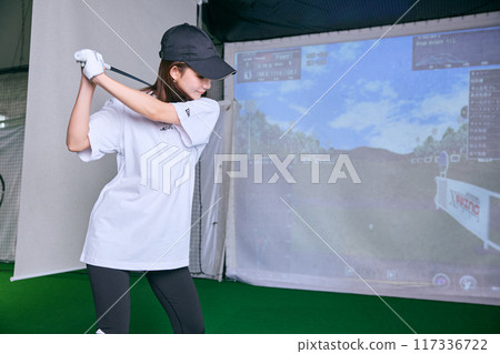 A woman practicing at an indoor golf driving range 117336722